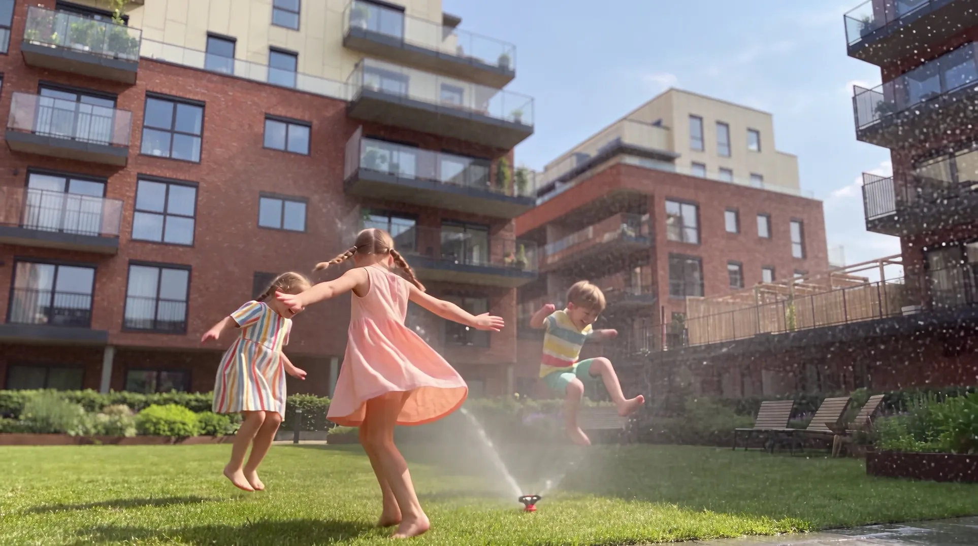 Children running through the garden sprinkler in summer